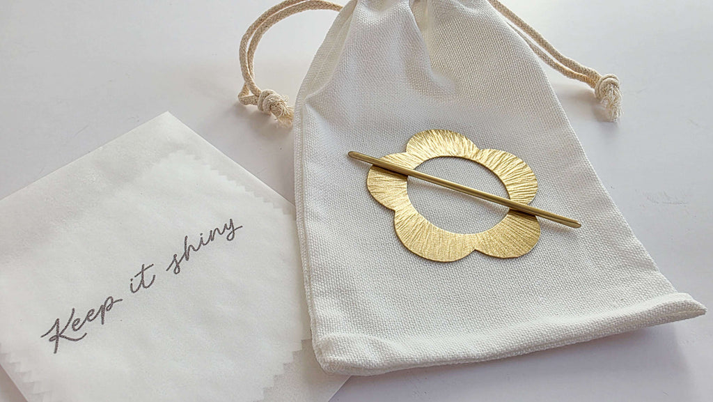 Gold hairpin on a white drawstring bag with 'Keep it shiny' text on a light gray background