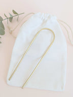 Brushed brass gold round pin hair fork - laid flat on a white drawstring cotton bag