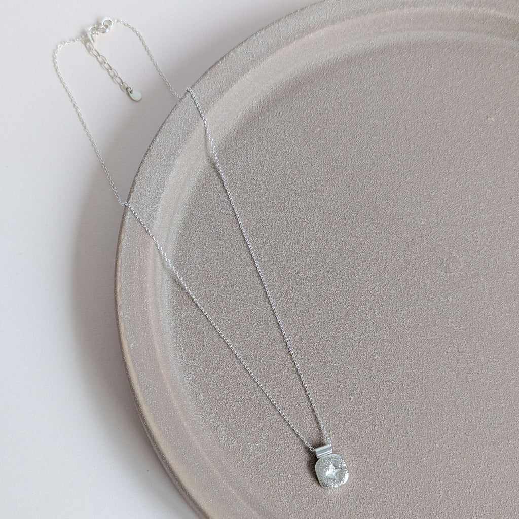 Silver star necklace with a clear pendant on a light gray plate