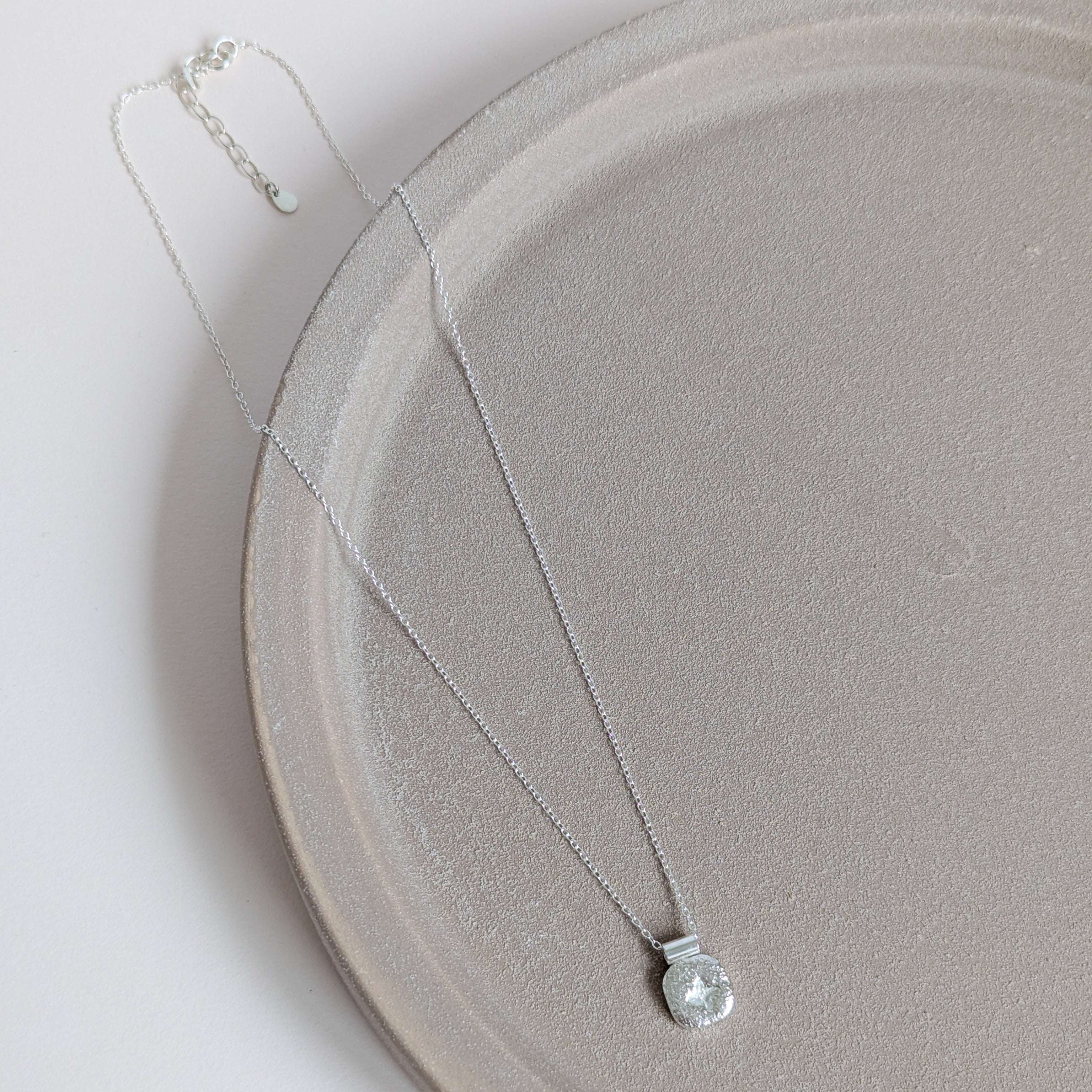 Silver star necklace with a clear pendant on a light gray plate