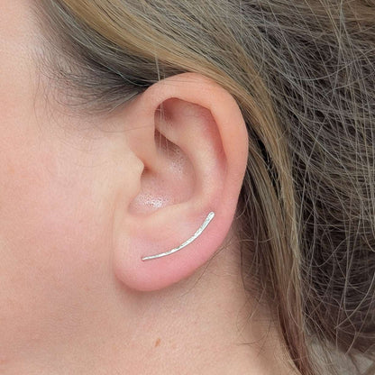 Close-up of an ear wearing a silver ear climber with hair partially covering the frame.