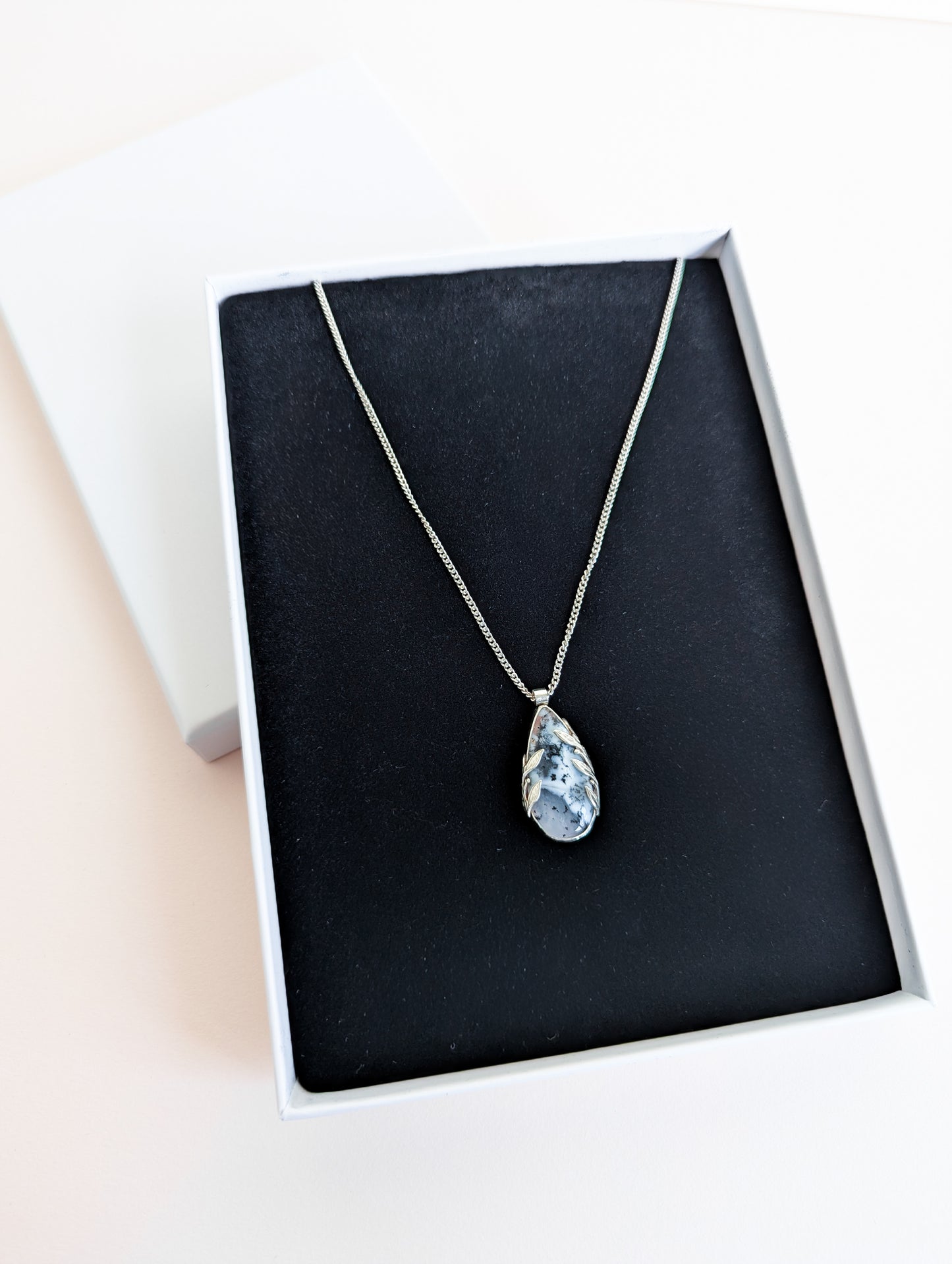 Dendritic snow agate leaf Necklace with a pendant in a white presentation box with black foam insert on a pink background