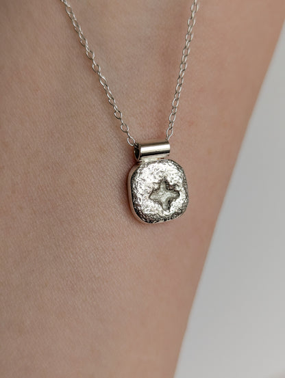 Silver square star necklace with a textured pendant on a person's neck against a neutral background