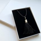 Black tassel necklace in a white box on a light background
