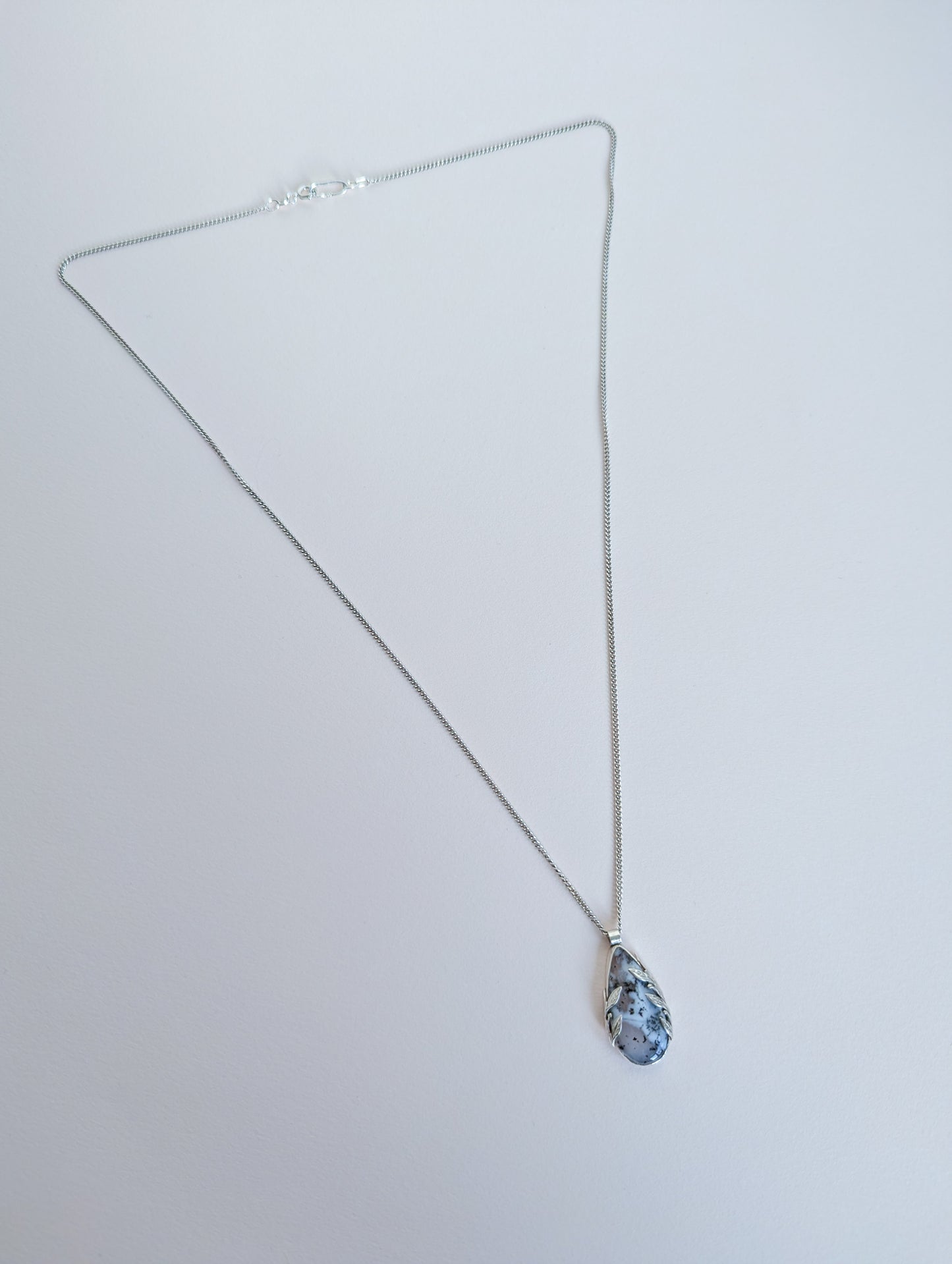 Dendritic snow agate leaf Necklace with a pendant on a light grey surface