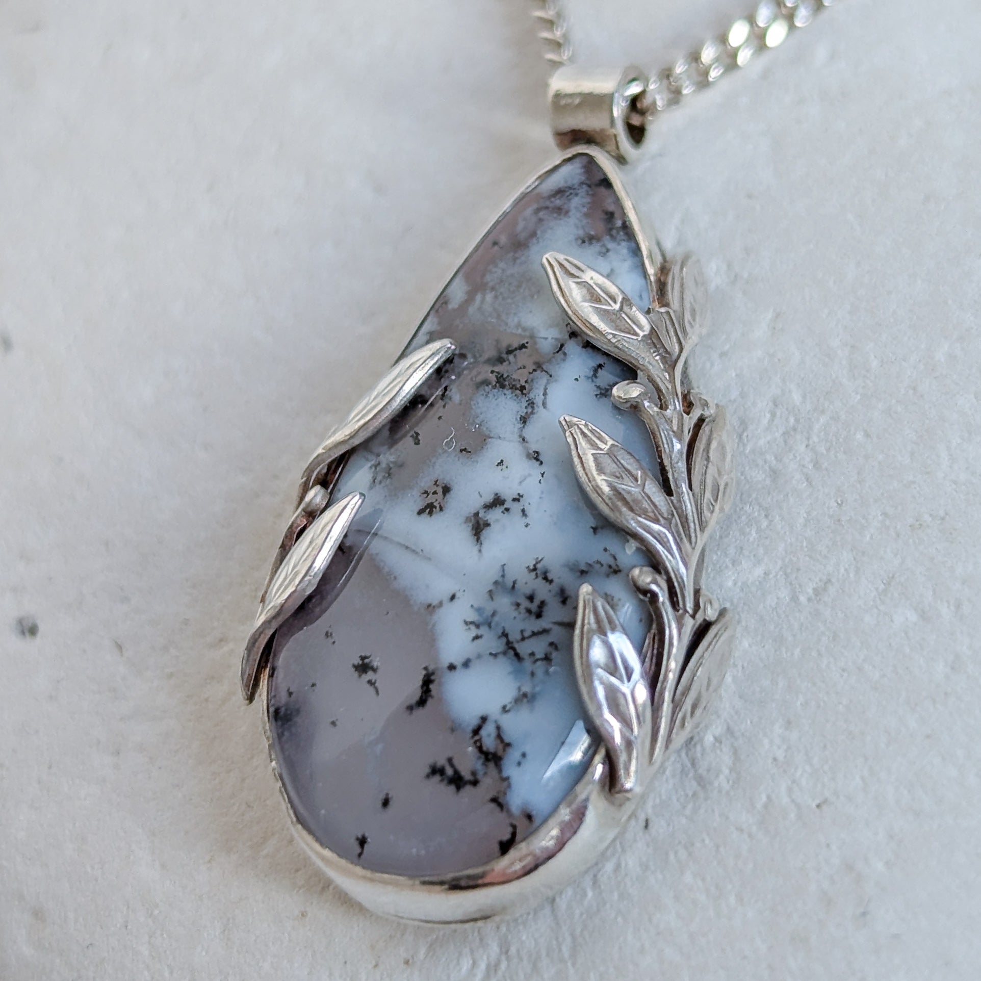 Dendritic snow agate leaf Necklace with a pendant on a light grey surface