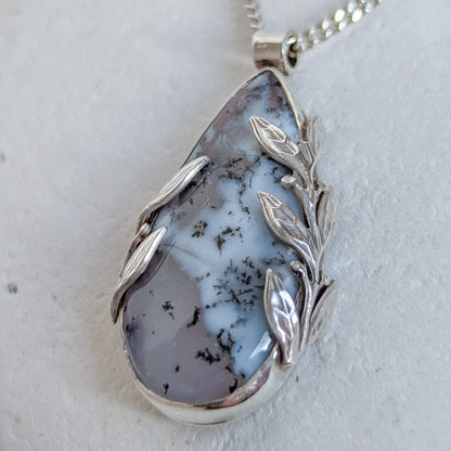 Dendritic snow agate leaf Necklace with a pendant on a light grey surface