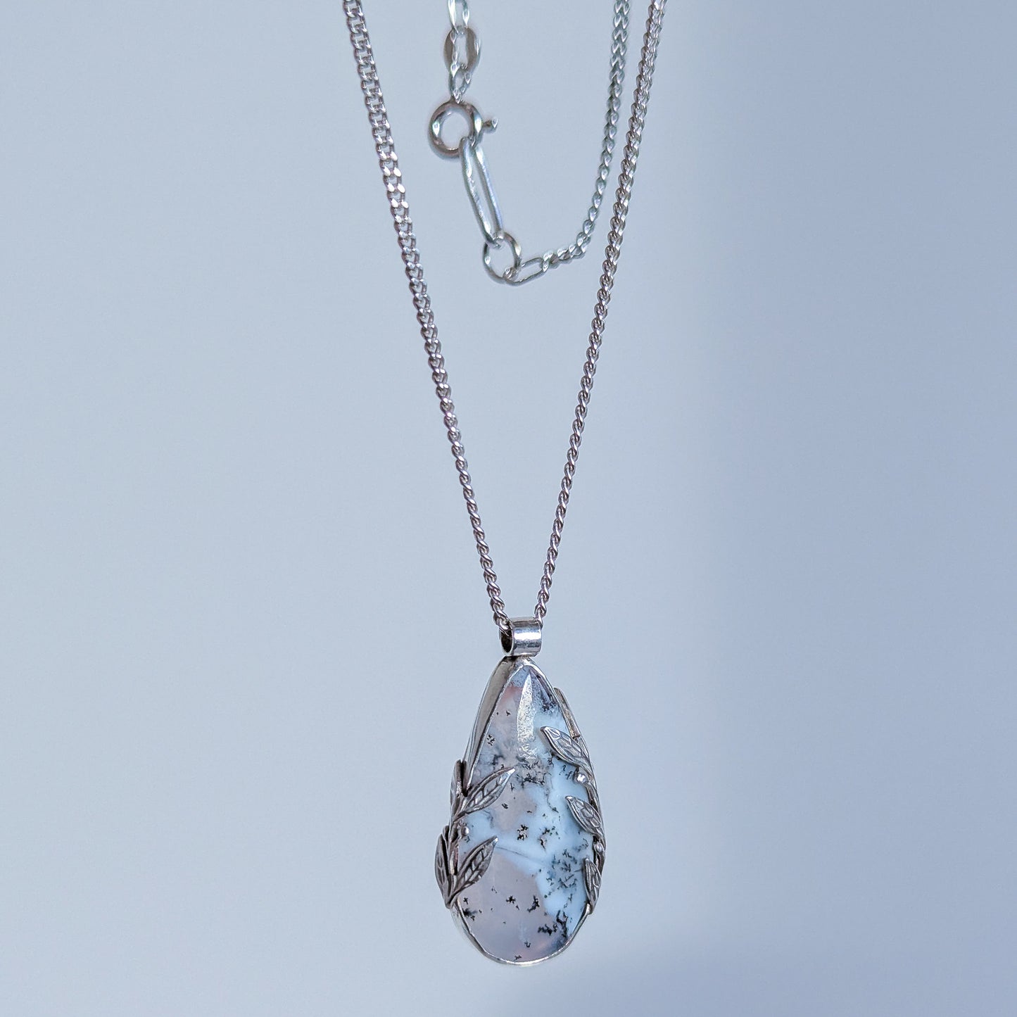 Teardrop-shaped pendant necklace with a textured design on a light gray background