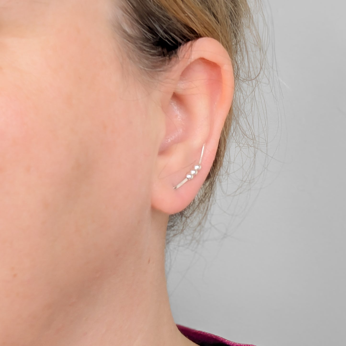Close-up of an ear wearing a silver  bead ear climber earring against a neutral background