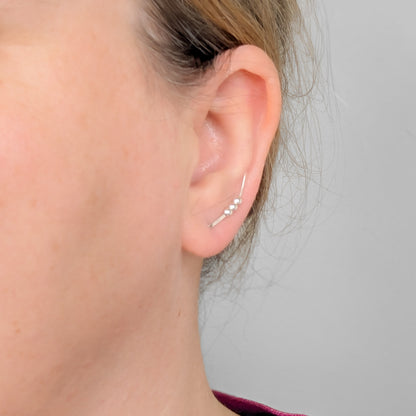 Close-up of an ear wearing a silver  bead ear climber earring against a neutral background
