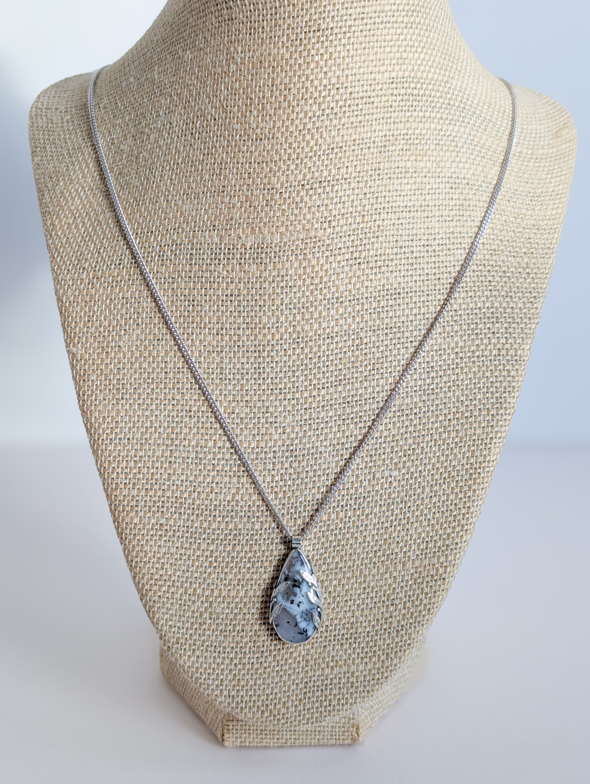 Dendritic snow agate leaf Necklace on a mannequin bust against a plain background