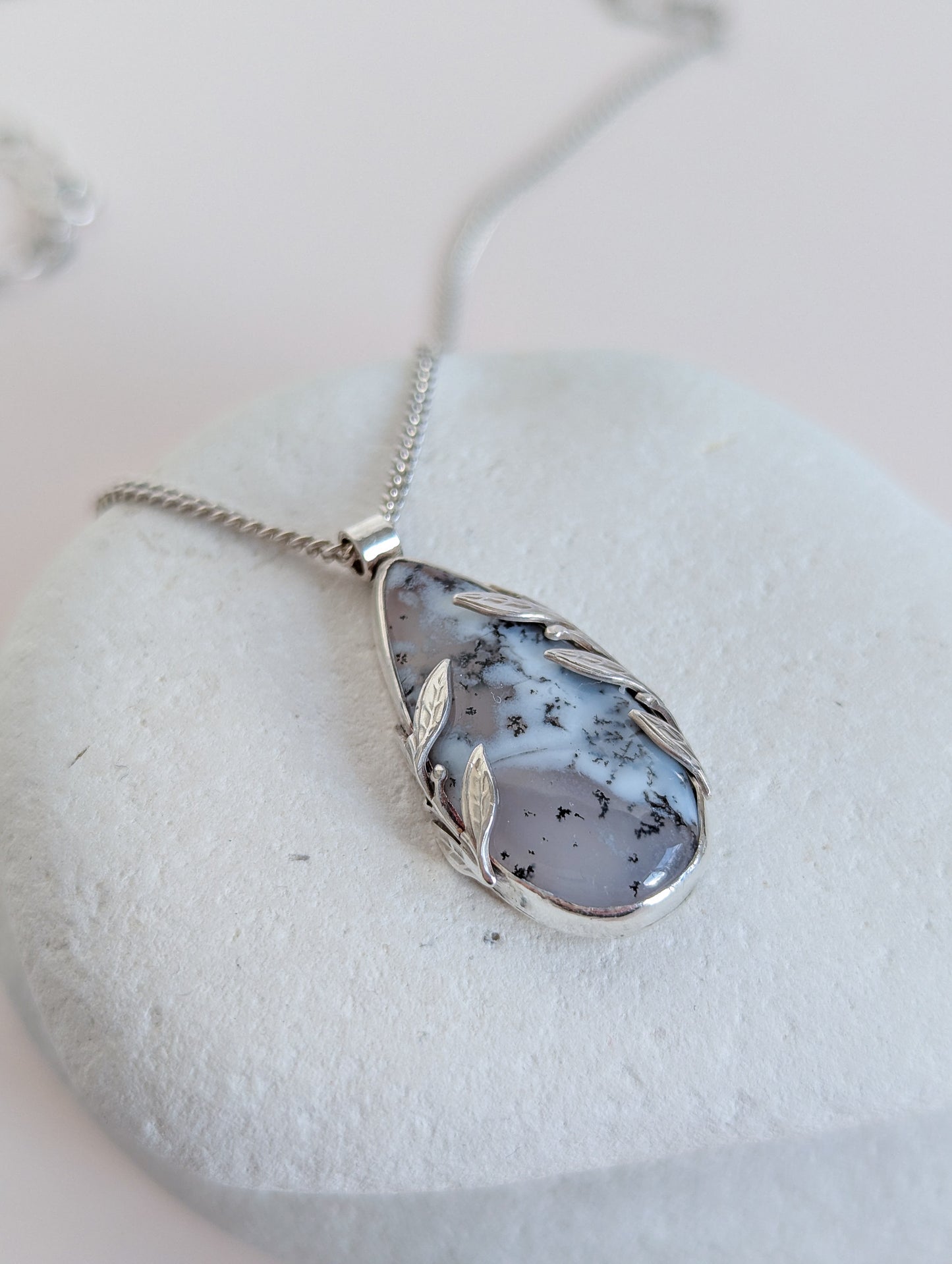 Dendritic snow agate leaf Necklace with a pendant on a light grey surface