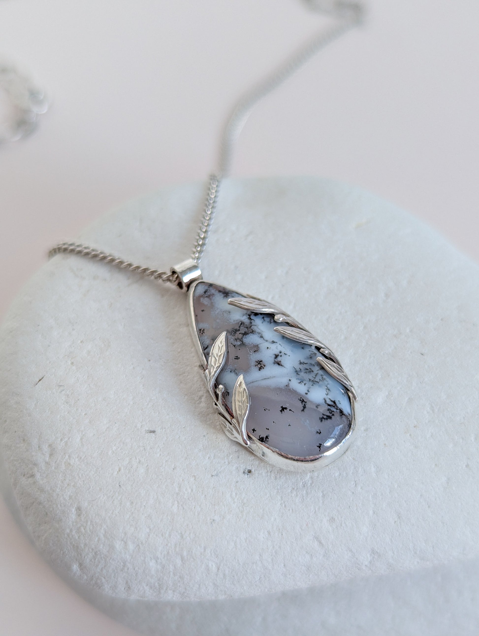 Dendritic snow agate leaf Necklace with a pendant on a light grey surface