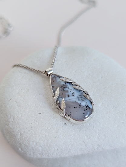 Dendritic snow agate leaf Necklace with a pendant on a light grey surface