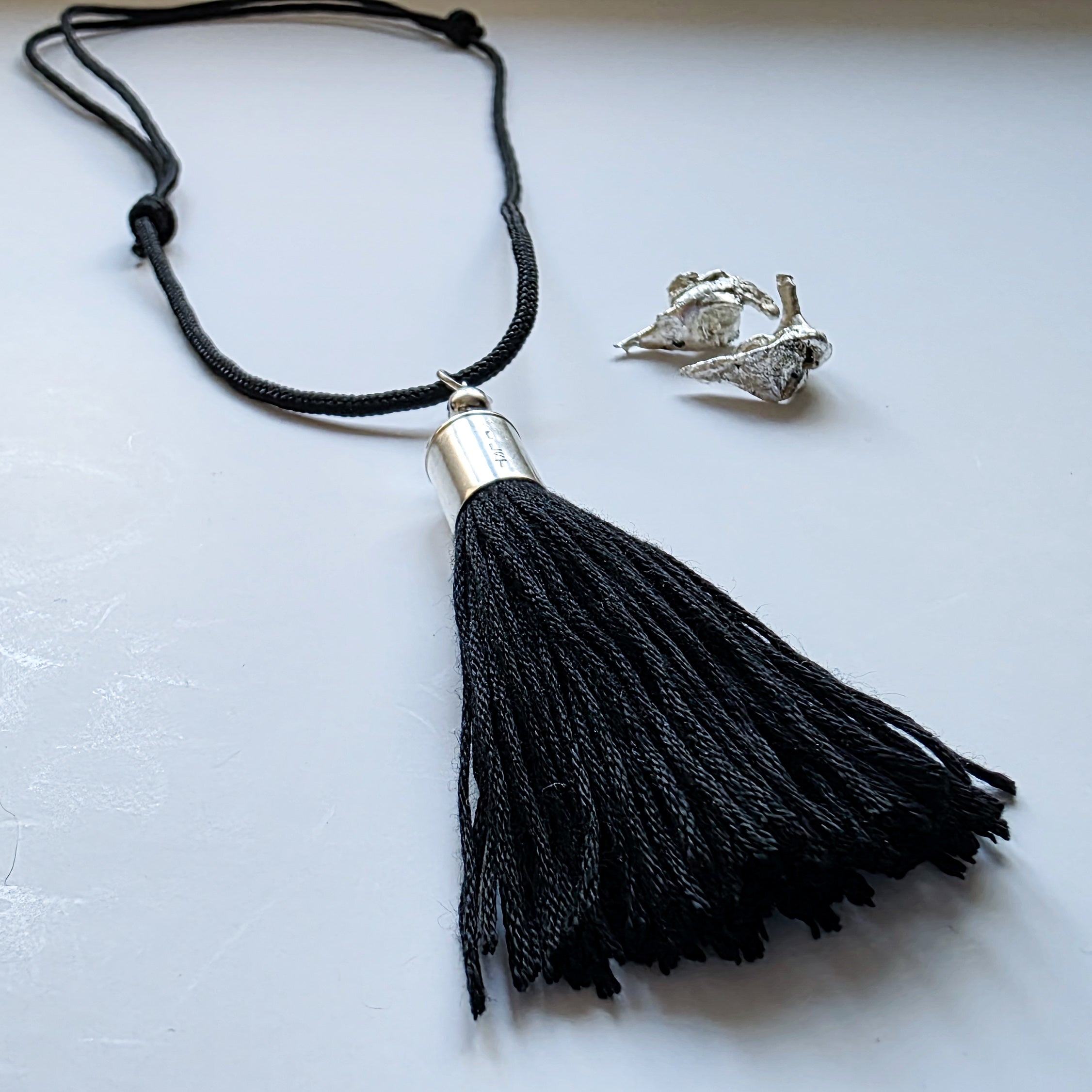 Black tassel necklace with silver pendant on a light gray background
