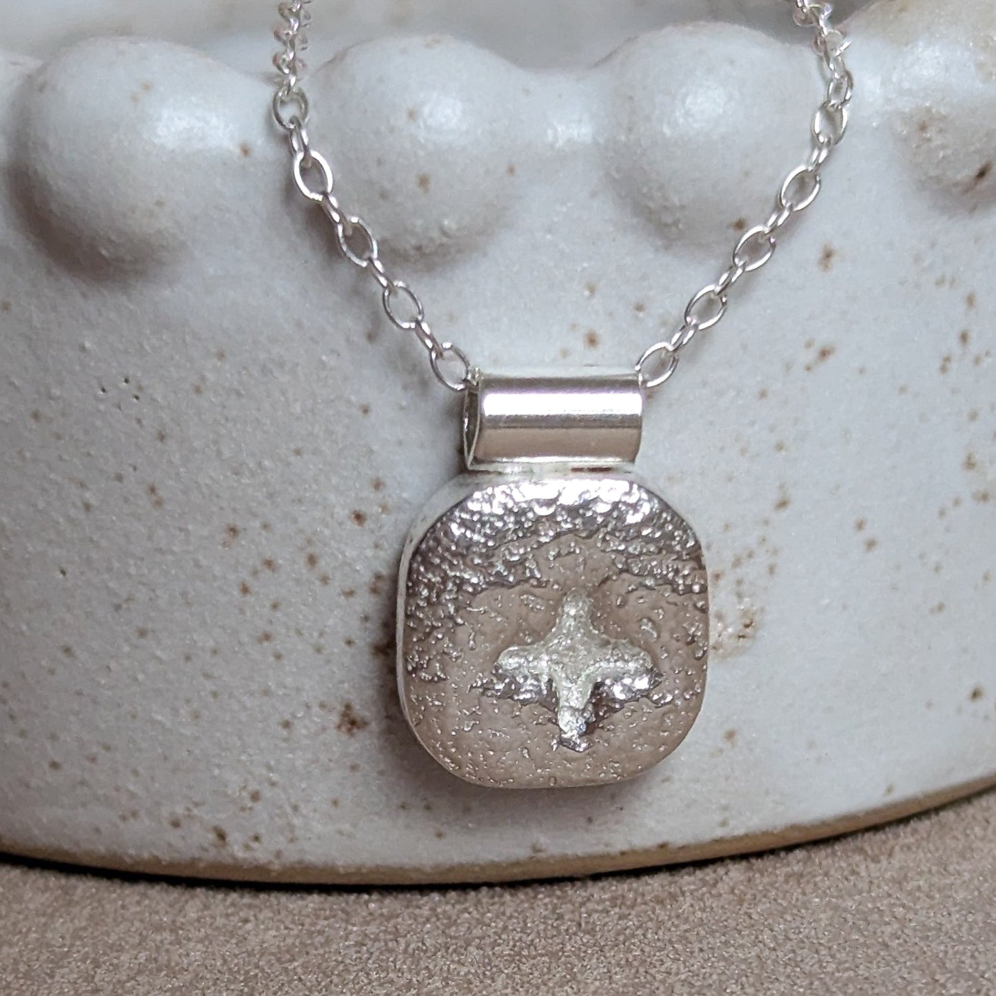 Silver pendant necklace on a textured white surface
