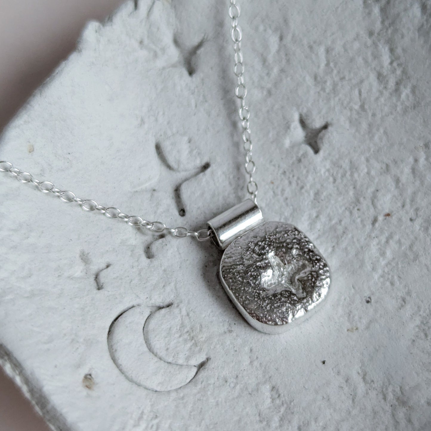 Silver square star necklace with a textured pendant on a textured surface