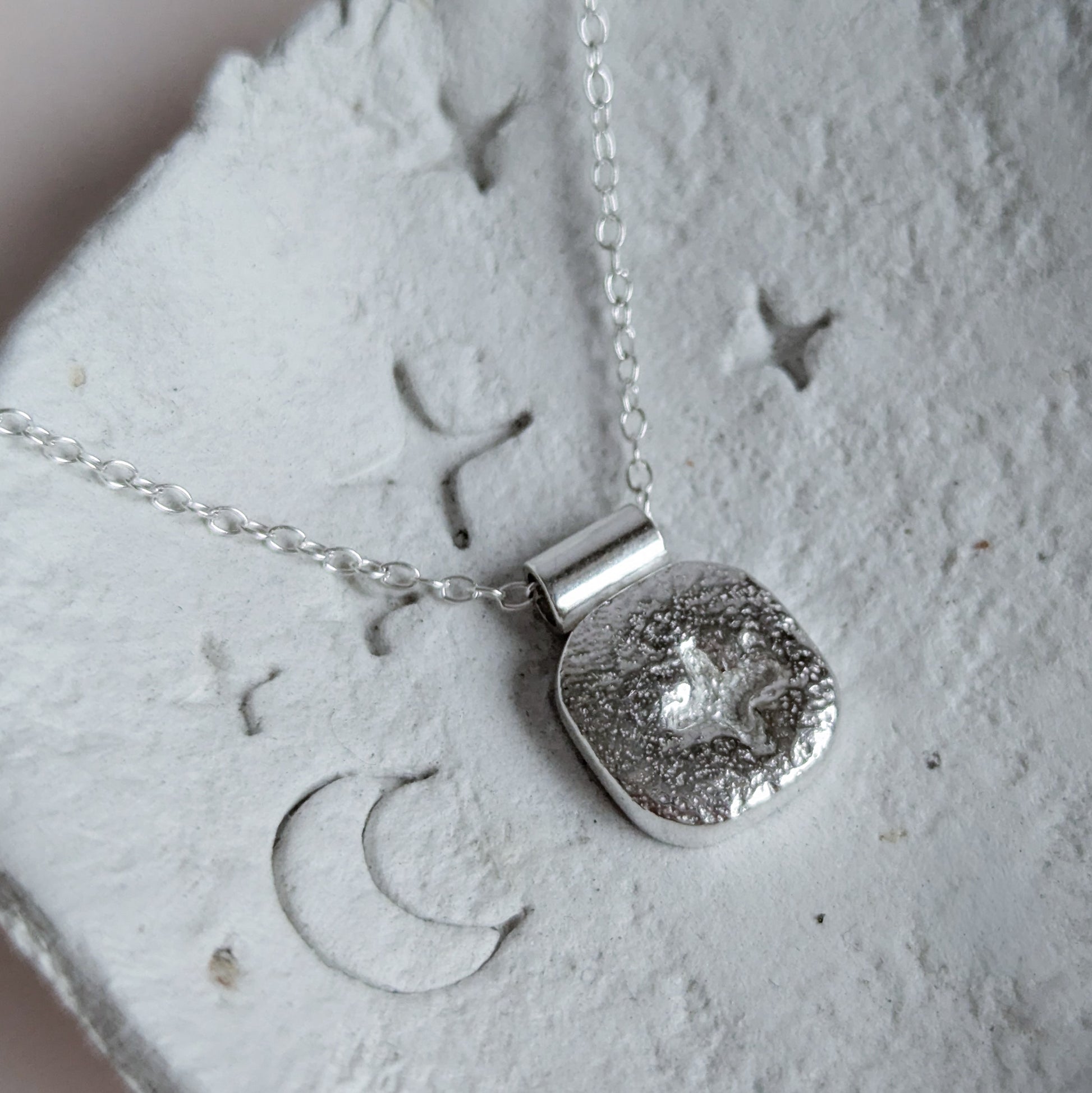 Silver square star necklace with a textured pendant on a textured surface