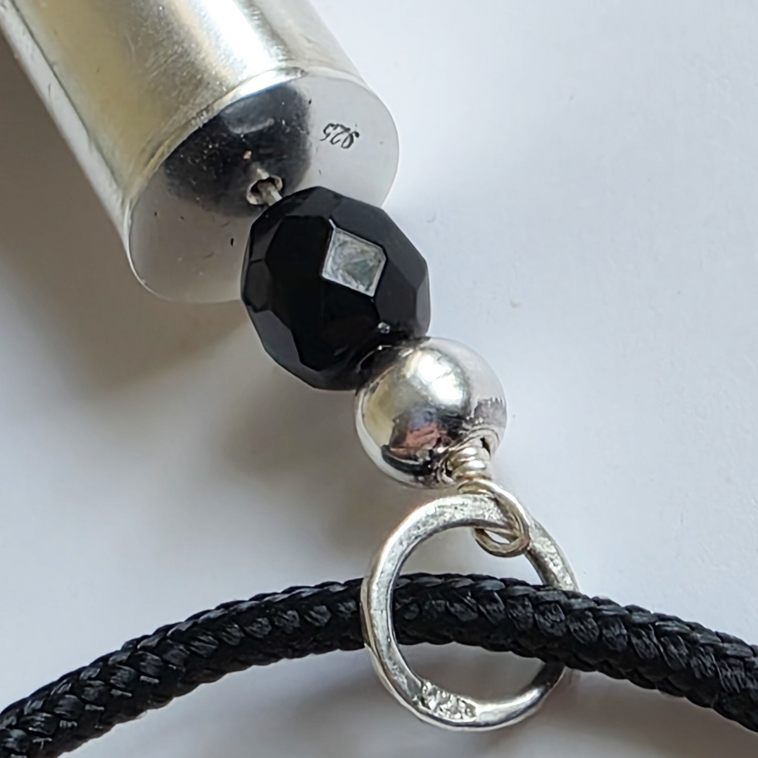 Close-up of a necklace with black bead and silver clasp on a white background
