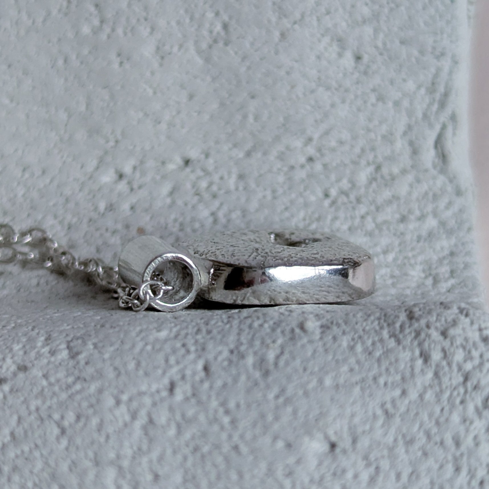 Silver pendant on a chain against a light gray background