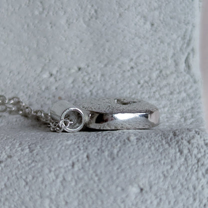 Silver pendant on a chain against a light gray background