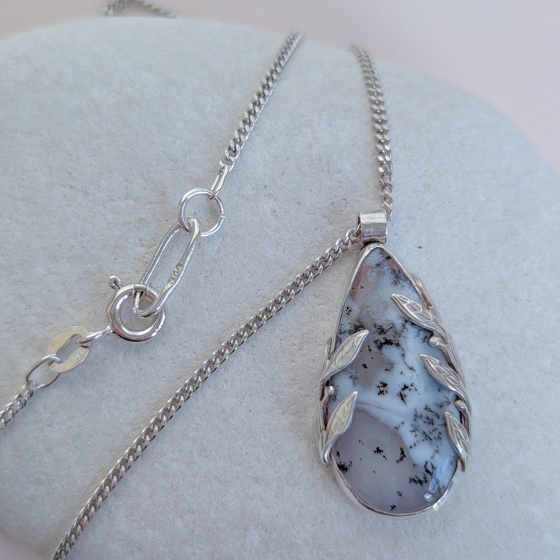 Dendritic snow agate leaf Necklace with a pendant on a light grey surface