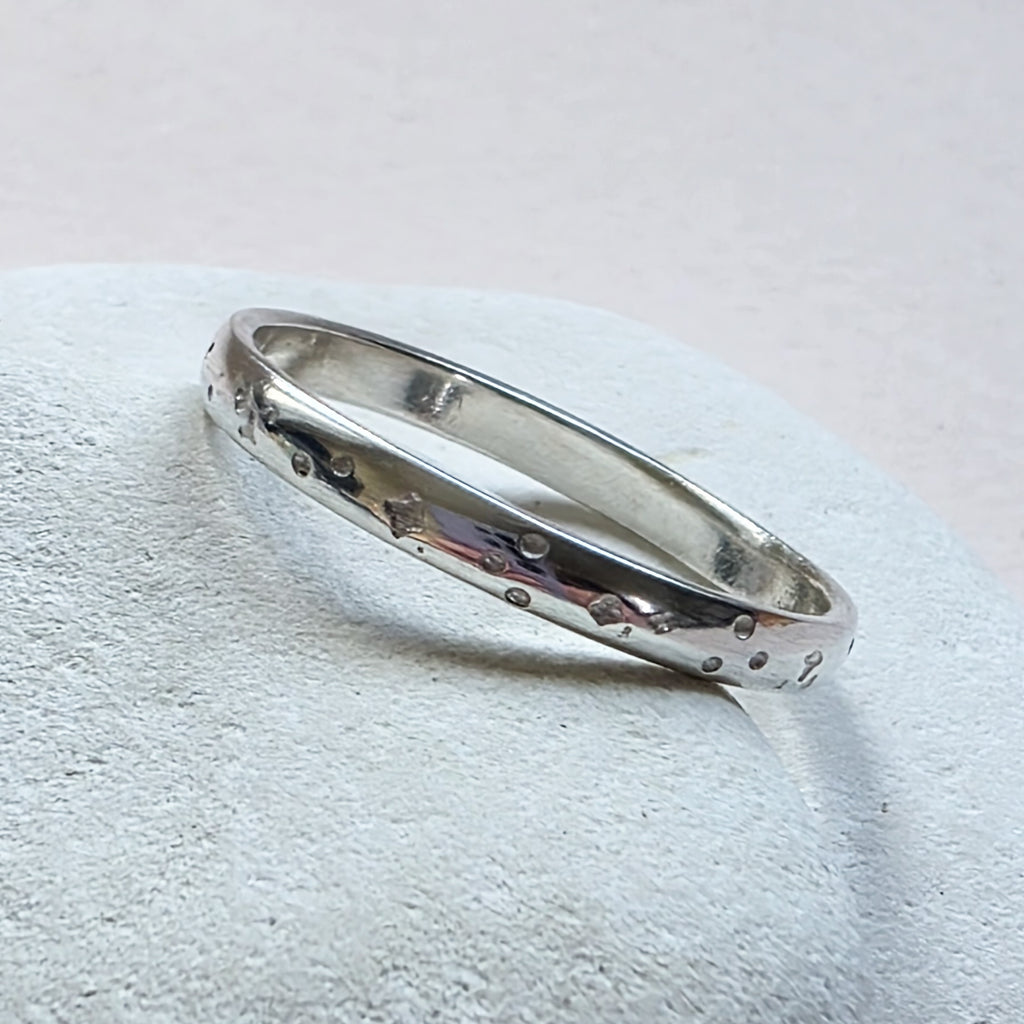 Sterling Silver ring with hand stamped star pattern on a light gray stone surface