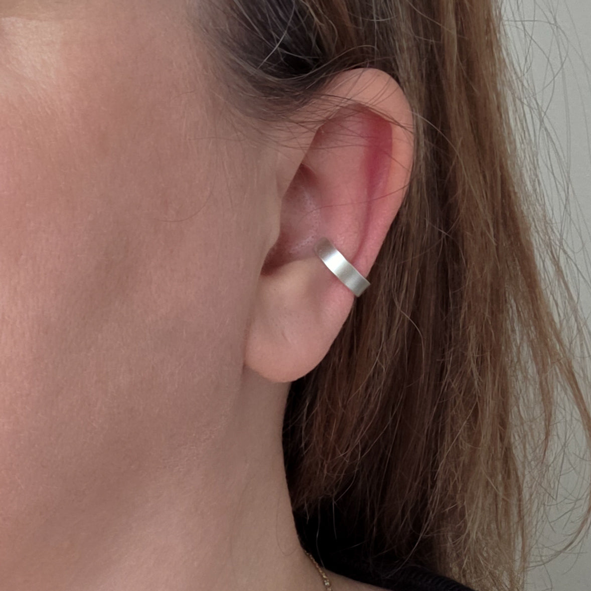 Close-up of an ear wearing a silver hoop earring with a neutral background