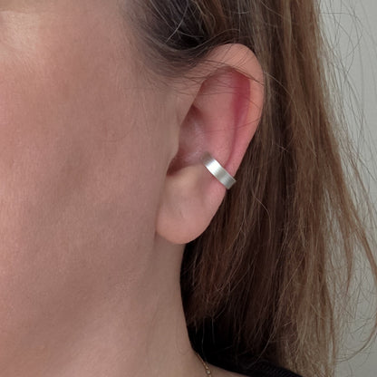 Close-up of an ear wearing a silver hoop earring with a neutral background