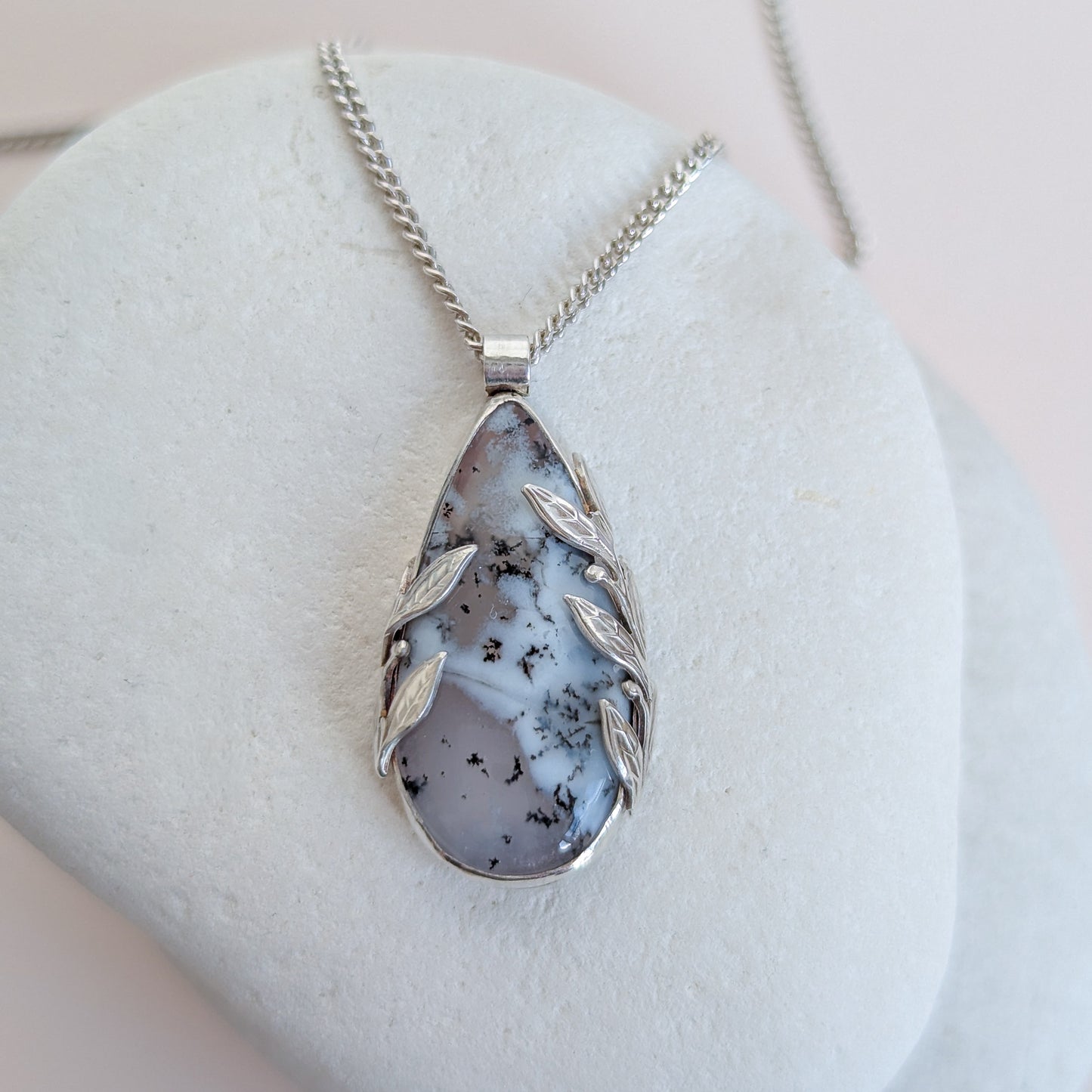 Dendritic snow agate leaf Necklace with a pendant on a light grey surface