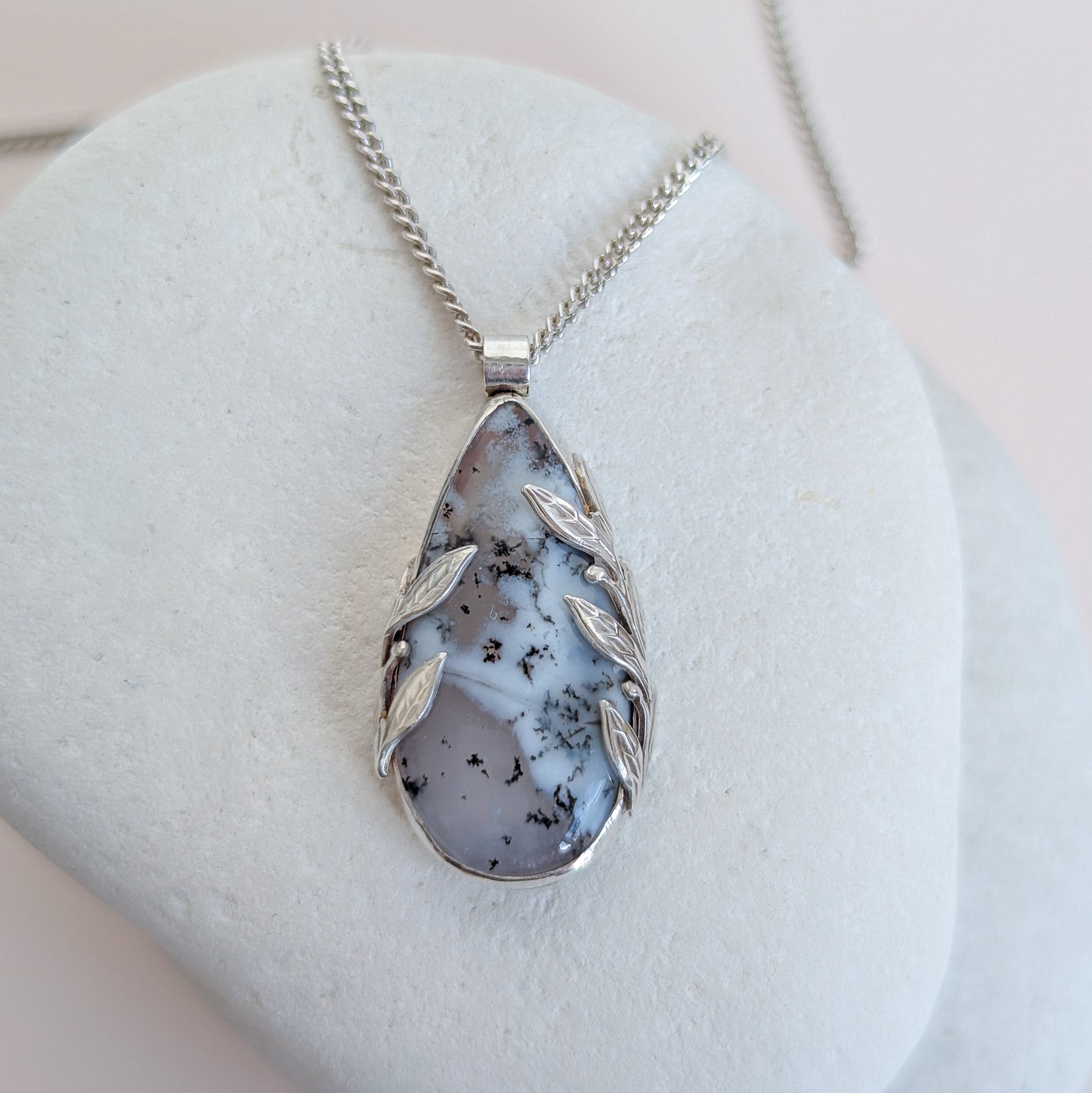 Dendritic snow agate leaf Necklace with a pendant on a light grey surface