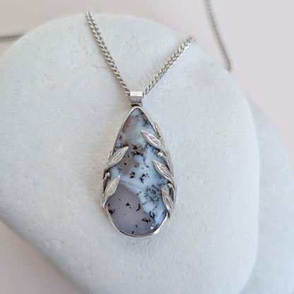 Dendritic snow agate leaf Necklace with a pendant on a light grey surface