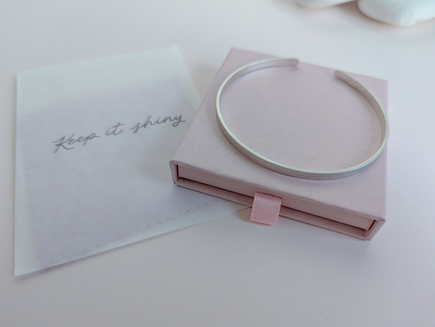 Silver bracelet in a pink box with a card that says 'Keep it shiny' on a light pink background