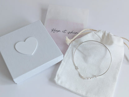 Thin sterling silver dainty cuff bangle with seed pearl bar chain - shows packaging including white drawstring cotton back, white jewellery presentation box with white wooden heart on the lid and polishing cloths