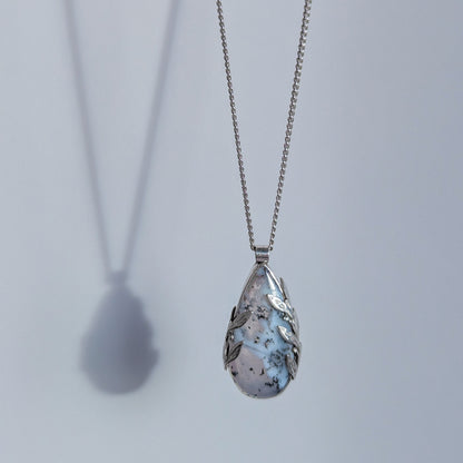 Dendritic snow agate leaf Necklace with a teardrop-shaped pendant on a light grey surface on a chain against a light grey background