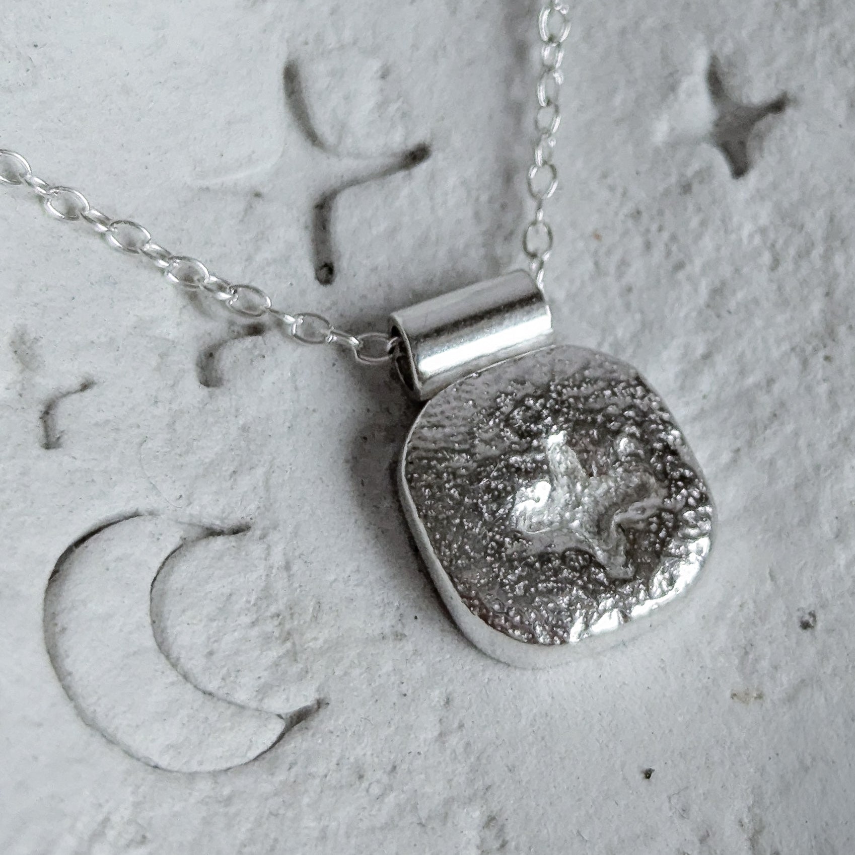 Silver necklace with a textured pendant on a textured surface
