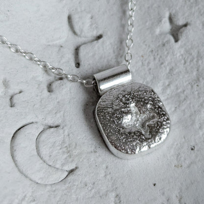 Silver necklace with a textured pendant on a textured surface