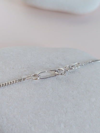 Silver chain necklace on a light gray surface with a neutral background