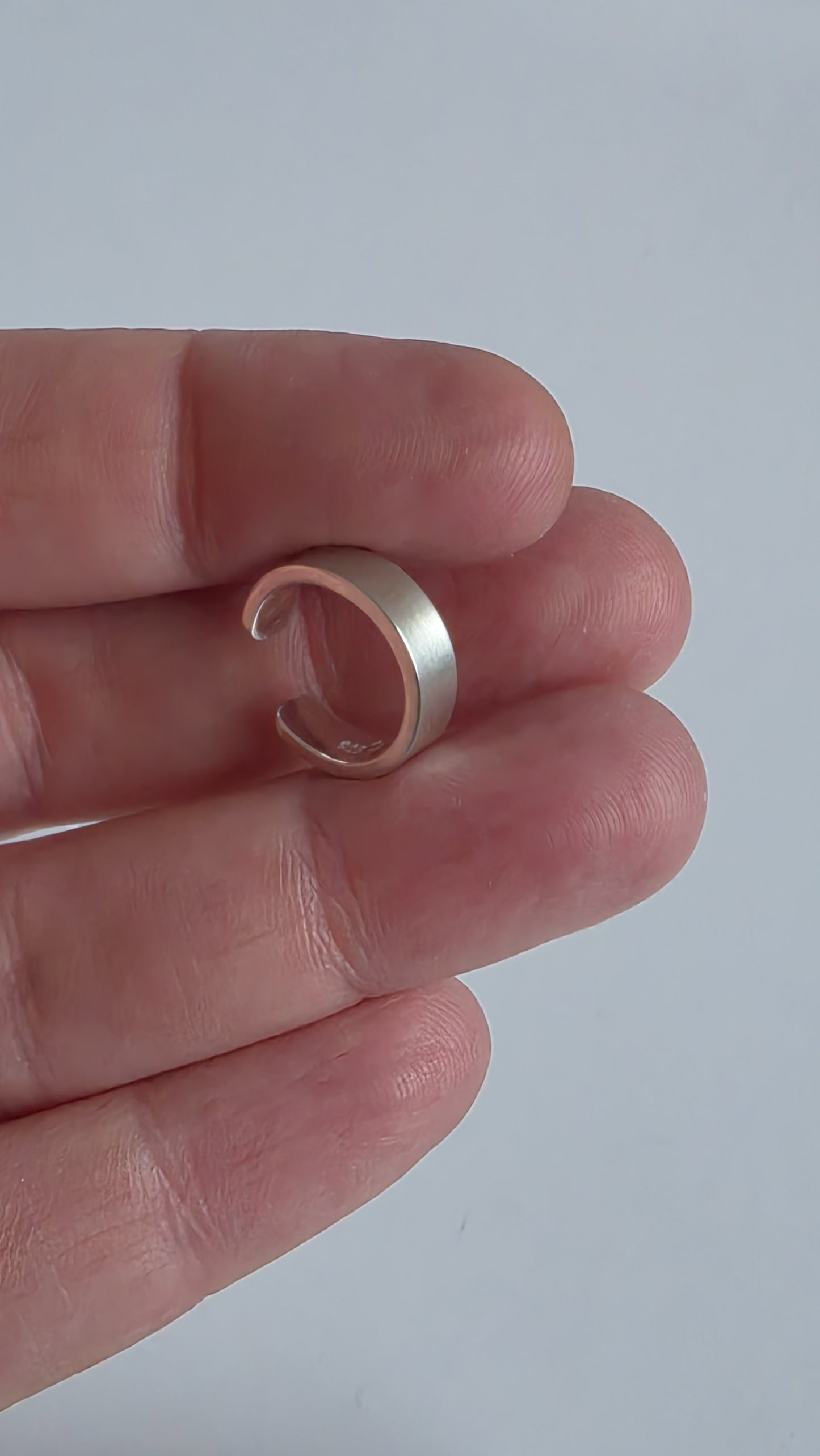 Silver ring held between fingers against a plain background