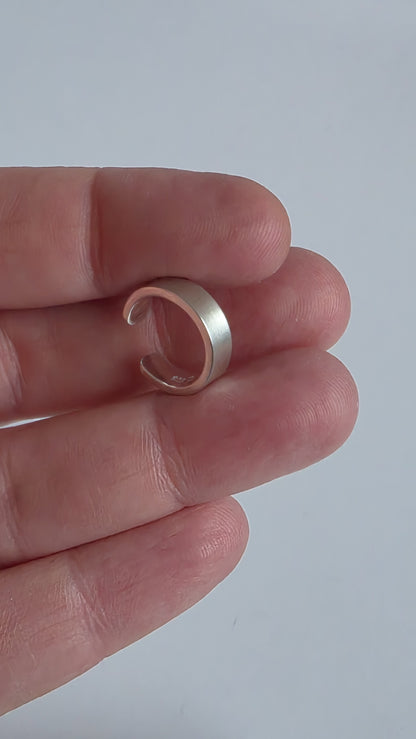Silver ring held between fingers against a plain background