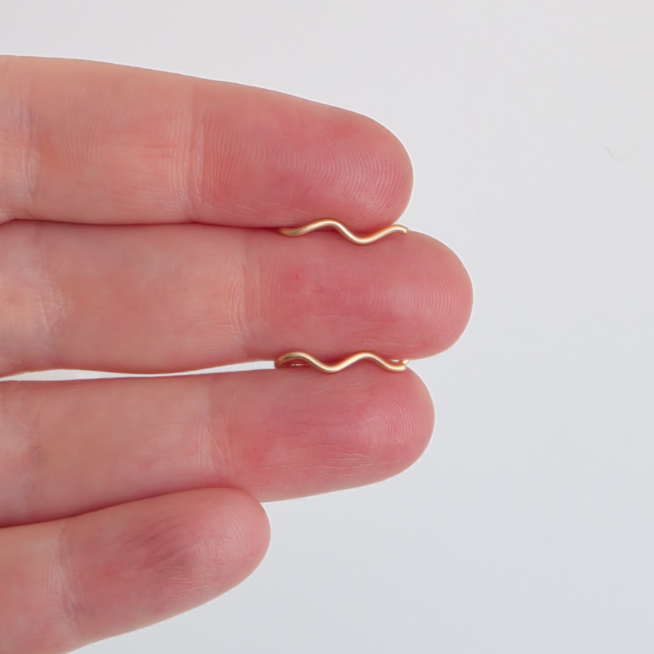 Gold wavy ear climber on a person's finger against a plain background - Wiggle Wave Sterling Silver + 14k Gold filled Ear Crawlers 