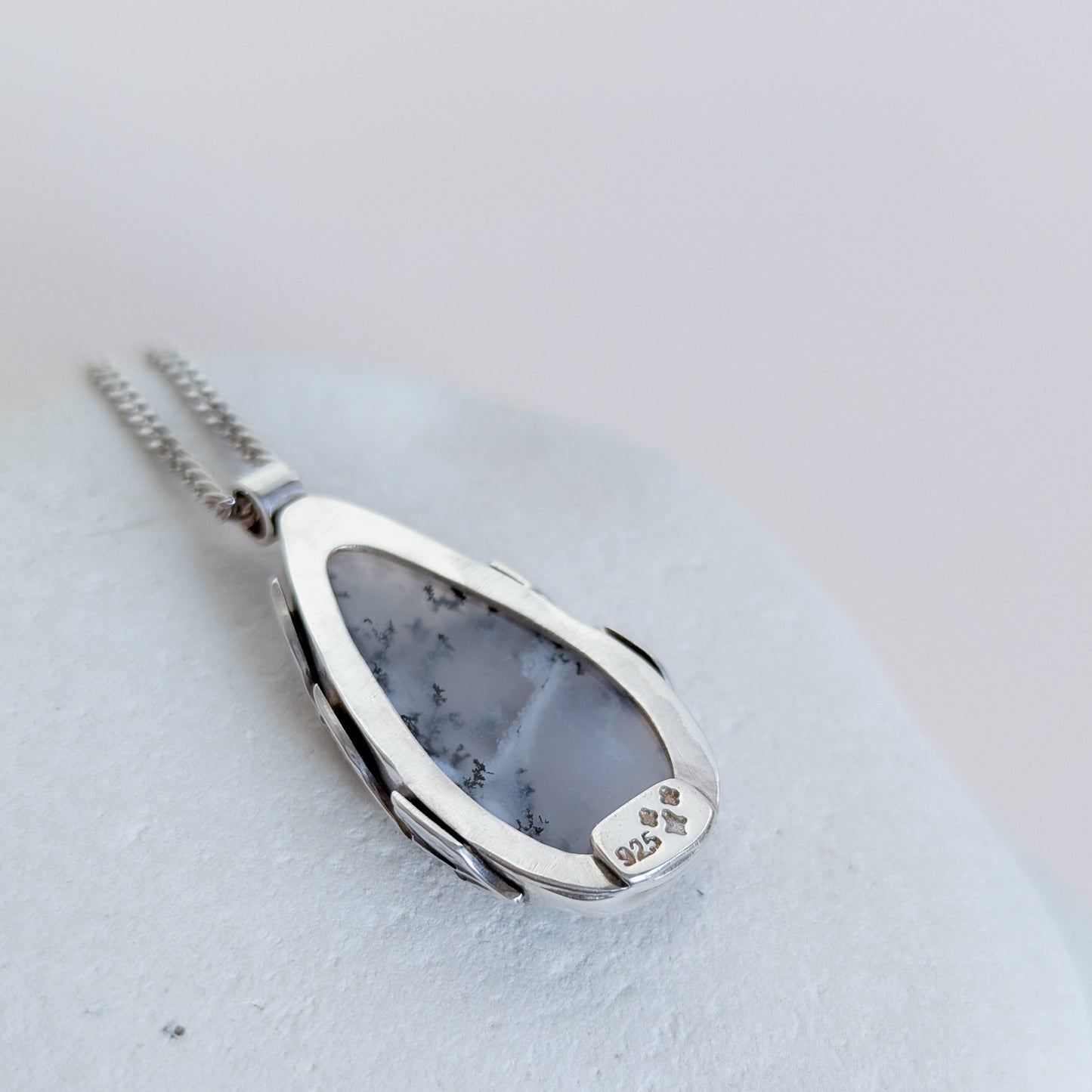 Dendritic snow agate leaf Necklace with a pendant on a light grey surface