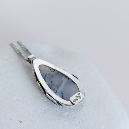 Dendritic snow agate leaf Necklace with a pendant on a light grey surface