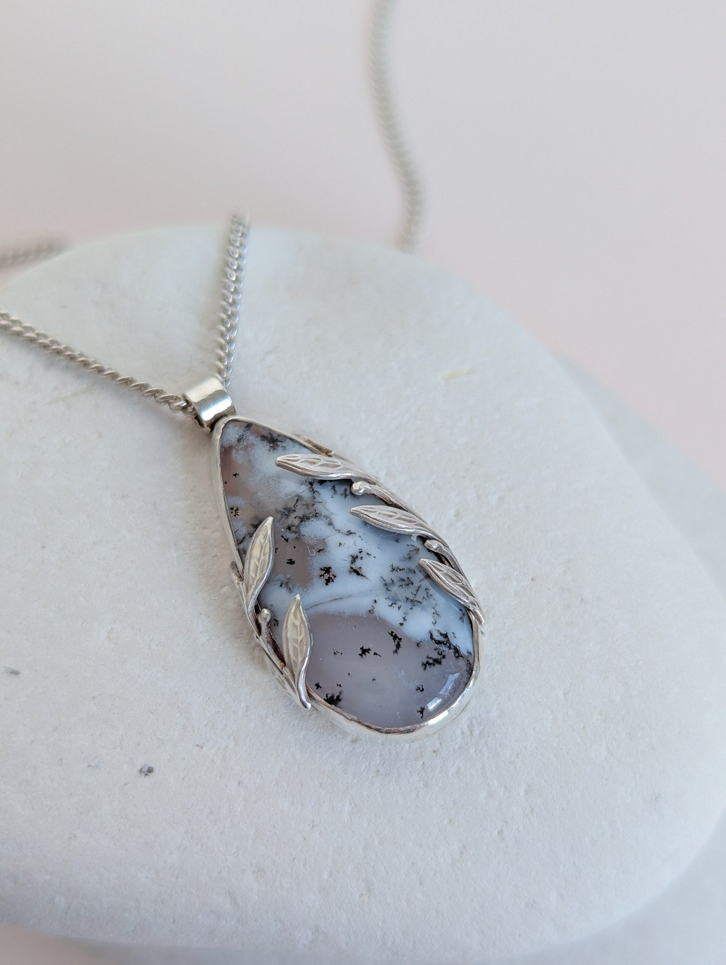 Dendritic snow agate leaf Necklace with a pendant on a light grey surface