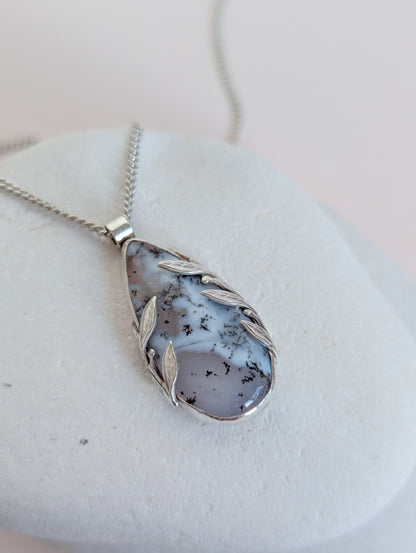 Dendritic snow agate leaf Necklace with a pendant on a light grey surface