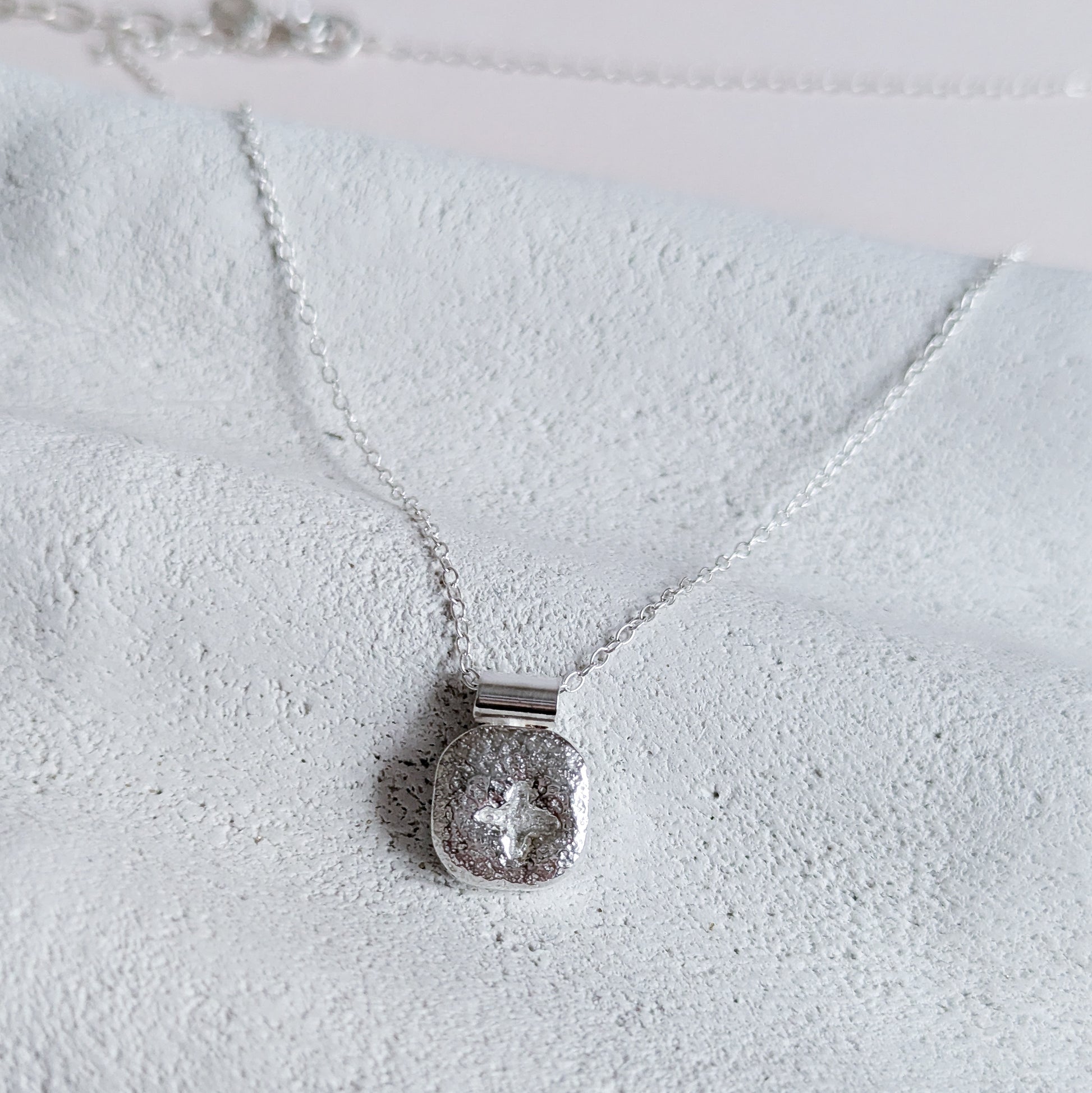 Silver necklace with a textured pendant on a textured white surface