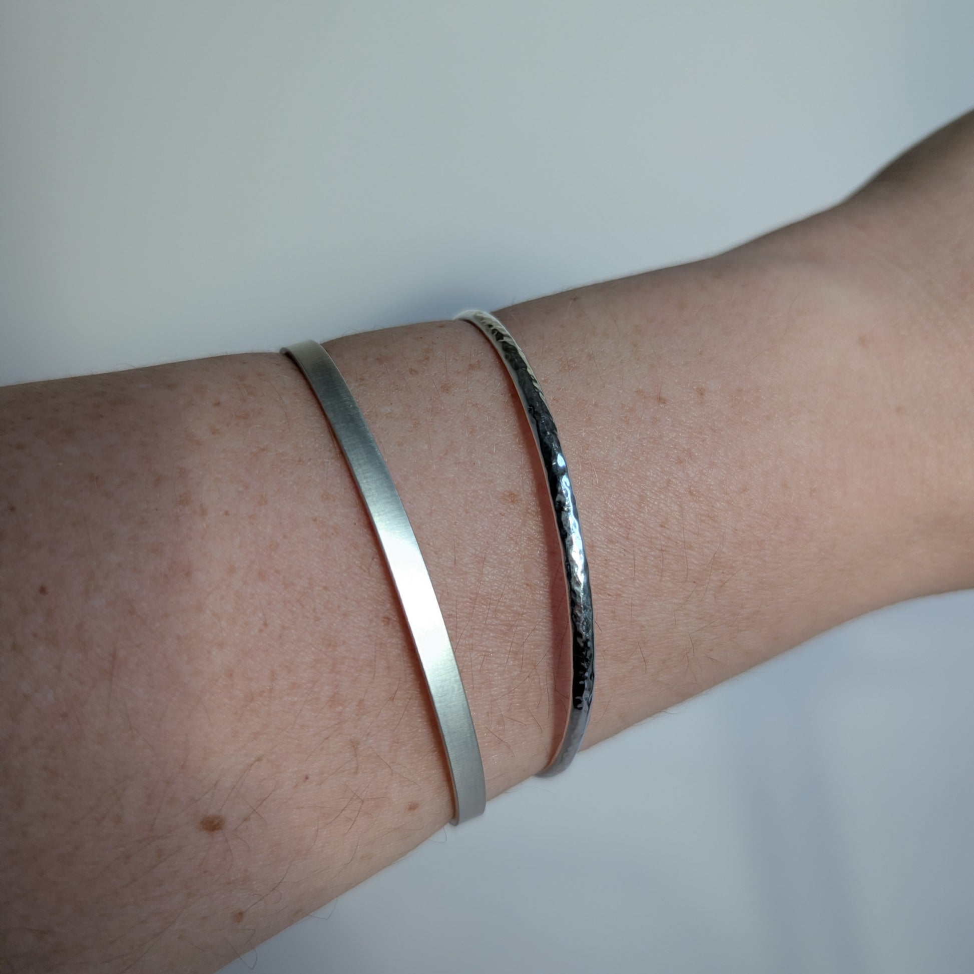 Two silver bracelets on a person's wrist against a light background