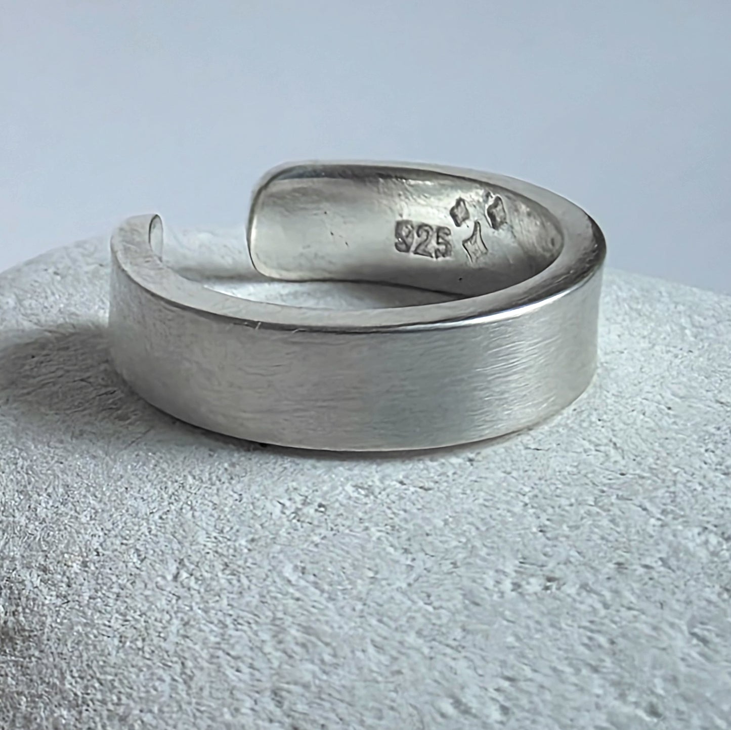 Silver ear cuff with '925' stamp on a textured surface