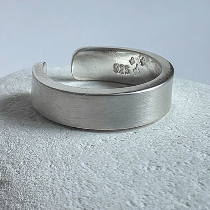 Silver ear cuff with '925' stamp on a textured surface