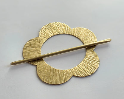 Gold hair clip with textured design on a light gray background